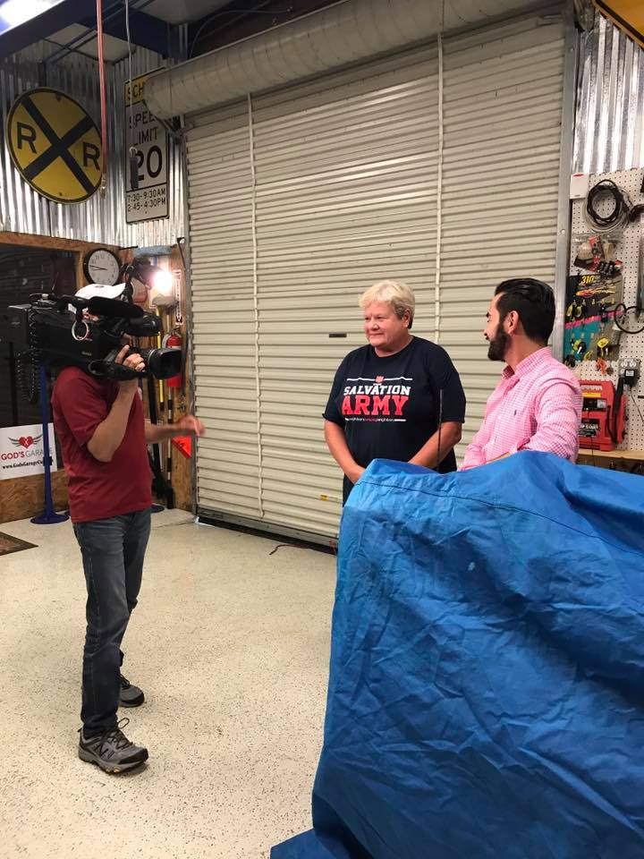 Camera crew interviewing a Salvation Army representative on the flake epoxy floor inside God’s Garage